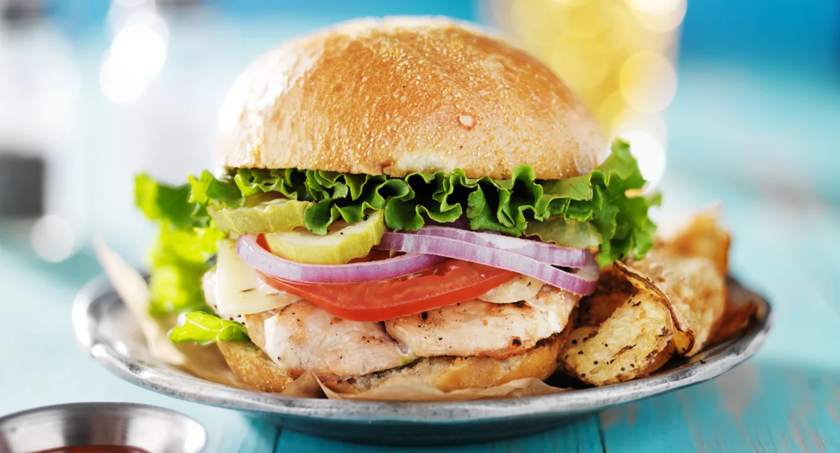 A grilled chicken sandwich with lettuce, tomatoes, onions, and cheese