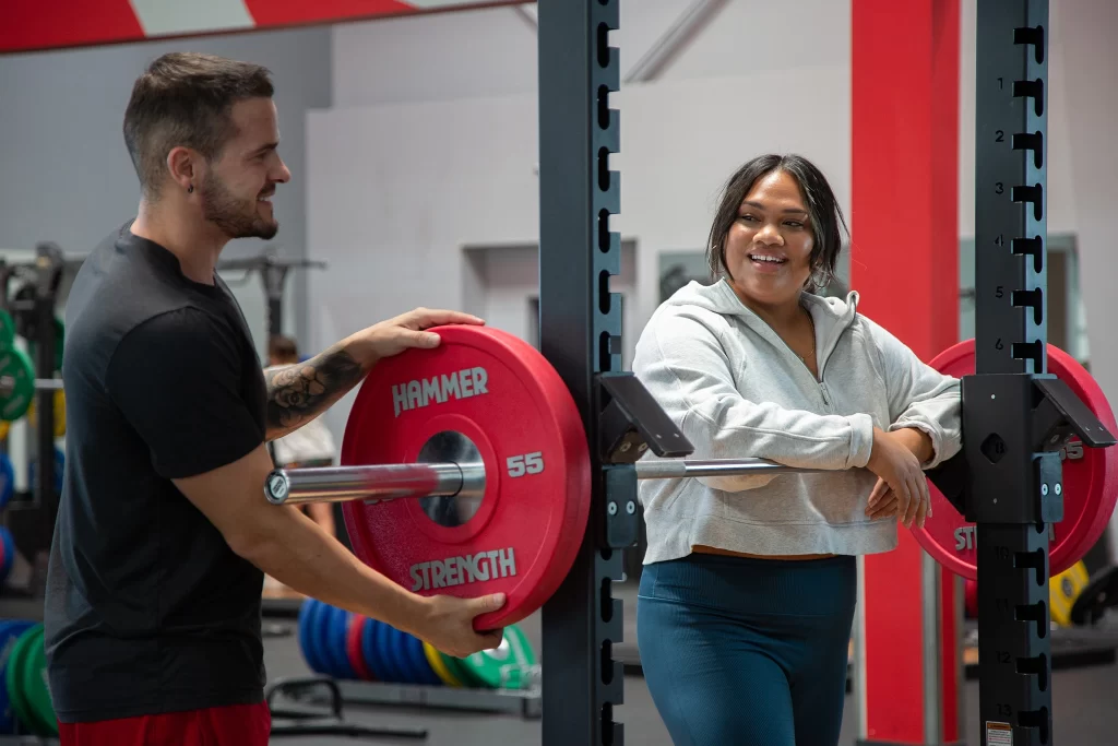 Male athlete putting weight onto a barbell for a female athlete at VASA Fitness