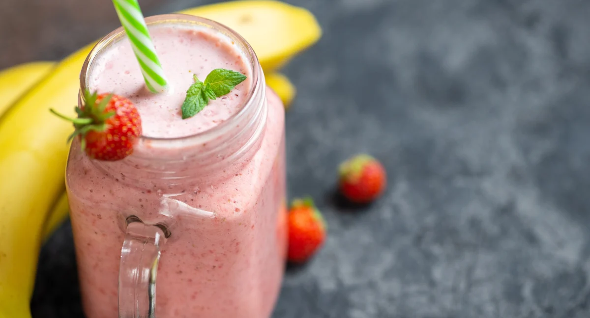 Strawberry banana smoothie in a glass jar mug with fresh fruit beside it